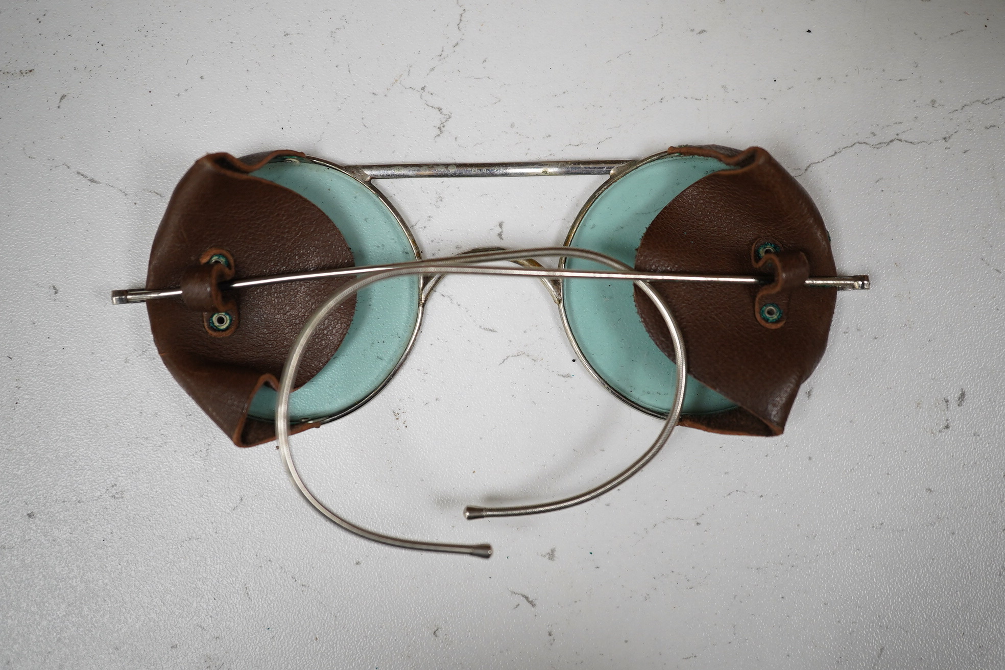 A cased pair of Air Ministry issue tinted glass spectacles with leather side attachments, case stamped; AM 294/11/P.1293, with sundry cloth badges. Condition - fair to good